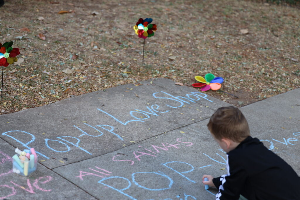 A child chalks Pop-up Love Shop on the sidewalk at All Saints'